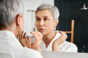 Senior woman with moisturizer on her face looking at mirror - cosmetic dermatology in aspen